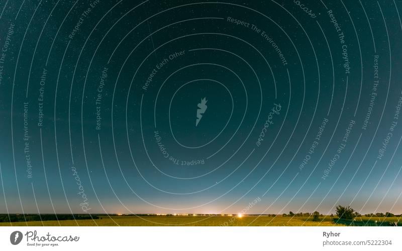 Nacht Sternenhimmel über Sommer Feld Wiese mit blühenden Raps. Glühende Sterne und Sonnenuntergang Sonnenaufgang Lichter über Wiese Landschaft.