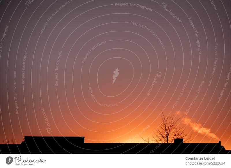 Sonnenuntergang über einem Dach mit rauchendem Schornstein. Natur Himmel Abend Qualm Rauch Umwelt Silhouette Klimawandel Energiewirtschaft Emission rot orange