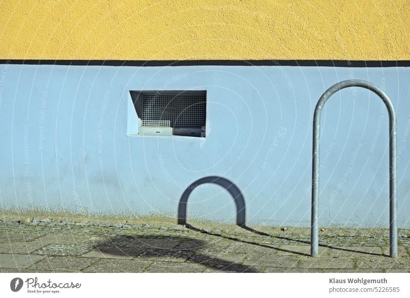 Schattenspiel an einer, farbig gestrichenen, sonnigen Hauswand. Ein Fahradständer wirft seinen Schatten an die Hauswand Licht Farben farbenfroh Kellerfenster