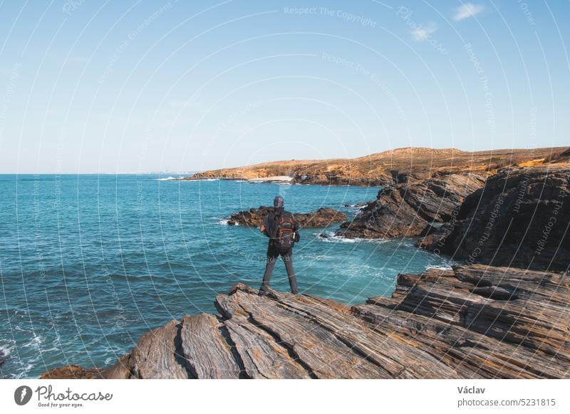 Ein älterer Mann mit einem Rucksack fotografiert die Schönheit der Atlantikküste bei Porto Covo, Portugal. Momente mit dem Mobiltelefon festhalten Senior reif