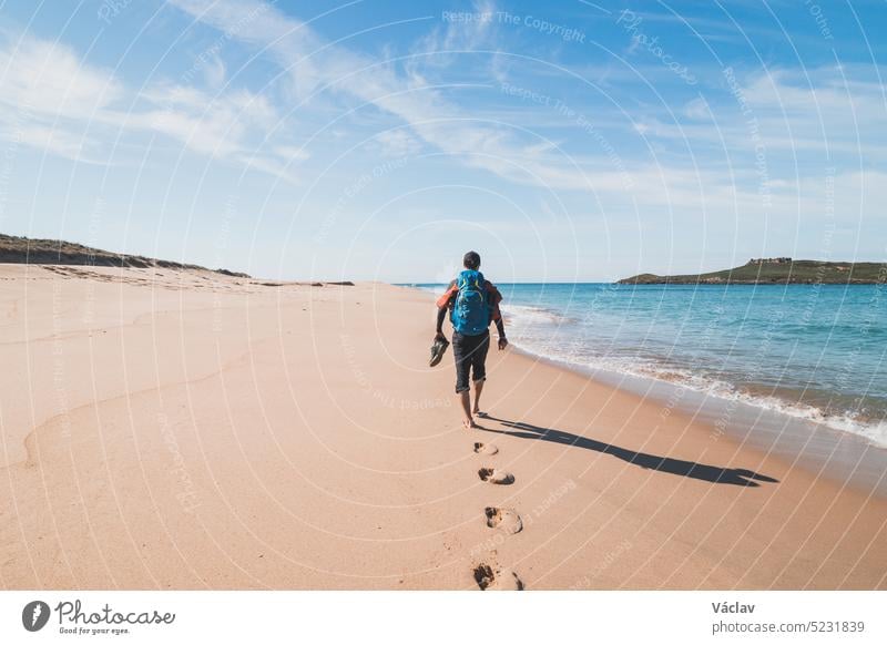 Leidenschaftlicher Rucksacktourist, Rucksack und Stiefel in der Hand, spaziert am Strand Praia da Ilha do Pessegueiro am Atlantik in der Nähe von Porto Covo, Portugal. Auf den Spuren der Rota Vicentina