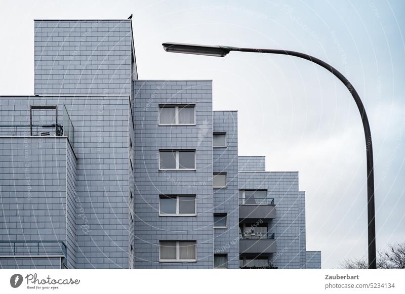 Lieber die Amsel auf dem Dach ... graues Mehrfamilienhaus in gestufter Architektur, harmonisch eingefasst von bogenförmige Straßenlampe Wohnhaus Lampe