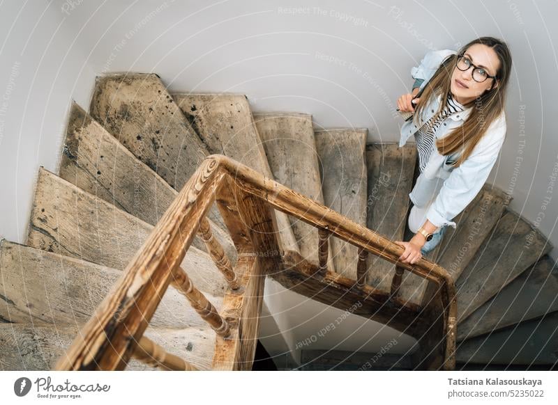 Eine Frau schaut auf einer alten Holztreppe stehend nach oben nachschlagen aufschauend Stehen hölzern Treppenhaus Menschen Person Erwachsener langhaarig allein