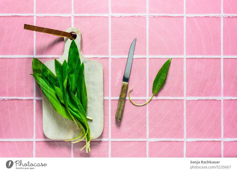 Frischer Bärlauch auf einem Schneidebrett. Rosa Kachel Hintergrund. frisch grün Kacheln rosa Draufsicht roh Gemüse Diät Zutaten Messer Essen zubereiten Holz