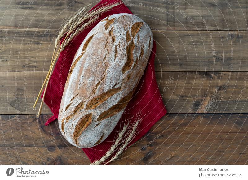 Ein Stück rustikales Brot auf einem hölzernen Hintergrund mit Ornamenten aus Weizenähren. Platz zum Kopieren. Lebensmittel Spielfigur Müsli Maiskolben