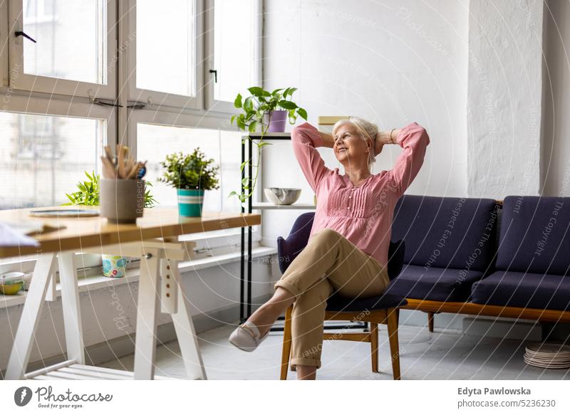 Entspannte ältere Frau, die am Tisch im Büro sitzt echte Menschen Senior im Innenbereich Loft Fenster heimwärts reifer Erwachsener eine Person attraktiv