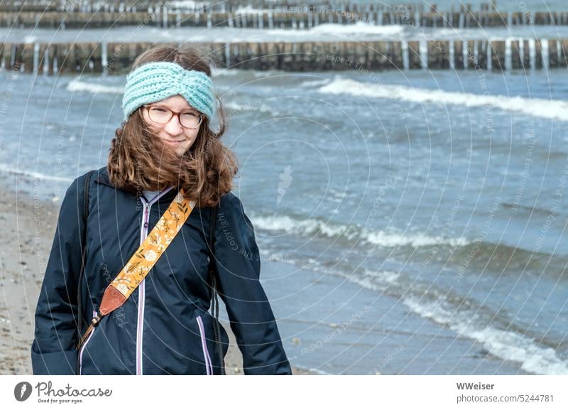 Das Mädchen lächelt, als es bei windigem Wetter die Ostsee-Küste entlangspaziert Wind junge Frau wandern spazieren laufen Haare Locken lächeln glücklich froh