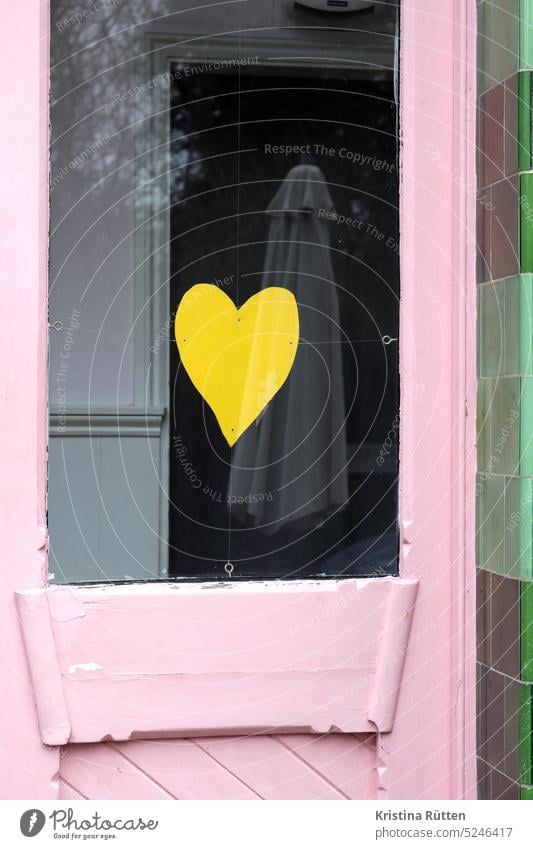 gelbes papierherz an rosa und grün symbol zeichen liebe fenster tür symbolisch glas. scheibe fensterscheibe spiegelung sonnenschirm bäume liebesgruß verliebt