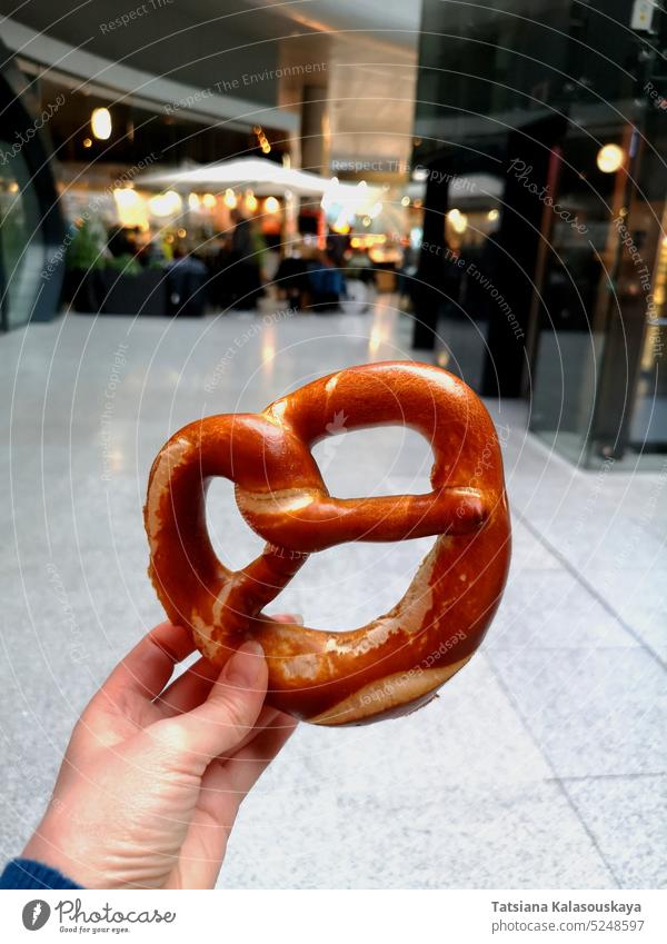 Eine Frauenhand hält eine traditionelle deutsche Brezel vor der Kulisse eines Cafés am Frankfurter Flughafen. Traditionelles deutsches Gebäck. Hand Lebensmittel