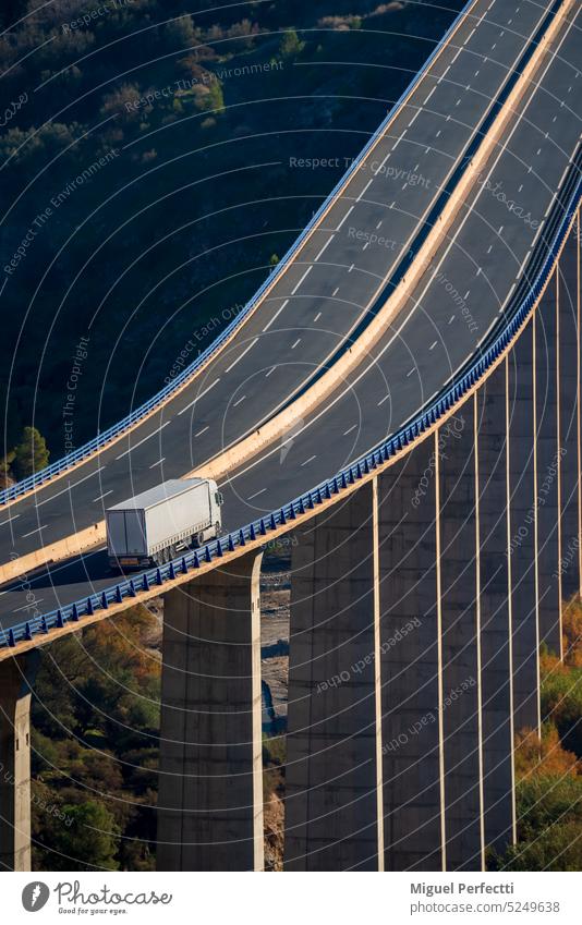 Lastkraftwagen mit Sattelauflieger für Stückgut, der über ein Viadukt mit großer Höhe über eine Schlucht fährt, Ansicht von oben. Autobahn Kurve Maschinenbau