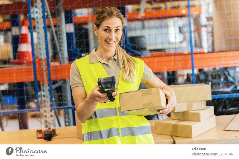 lächelnde Mitarbeiterin mit Schutzweste und Scanner, die in einen Paketscanner tippt, stehend im Lager einer Speditionsfirma Kasten Lagerhalle glückliche Frau