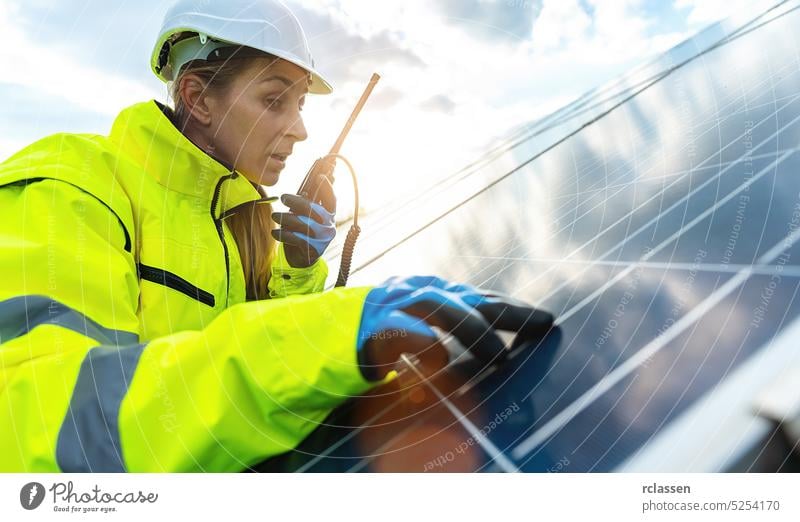 Weibliche Ingenieurin spricht in einem Walkie Talkie, um ein Solarpanel Feld zu kontrollieren und sieht glücklich aus. Nachhaltige Energie und Solarenergie Feld Konzept Bild