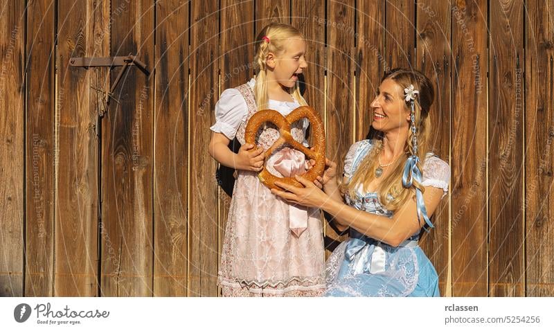 Mutter und Tochter halten Milchkannen in traditioneller bayerischer Tracht auf einem Bauernhof in Bayern auf einem Holzhintergrund. Oktoberfest Konzeptbild