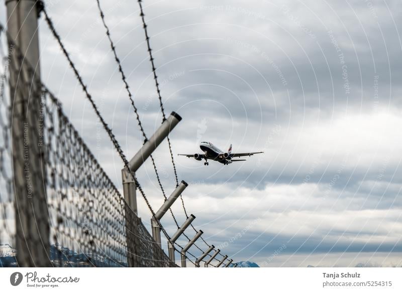 Flugzeug im Landeanflug über dem Stacheldraht Landung Zaun Bewölkt Passagierflugzeug Flughafen Grenze Begrenzung Luftverkehr fliegen Außenaufnahme Himmel Wolken