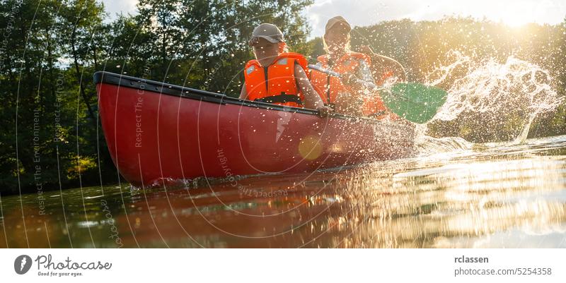 Kind mit Mutter und Vater in einem Kanu auf einem Fluss. Sommercamp für Kinder. Kajak- und Kanufahren mit der Familie. Kinder im Kanu. Familie auf Kajakfahrt. Wilde Natur und Wasserspaß im Sommerurlaub.