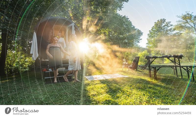 Vier Freundinnen kommen bei Sonnenuntergang aus einer Holzfass-Sauna. Sie sind entspannt und genießen die kühle Luft, während sie in der finnischen Saunakabine relaxen.