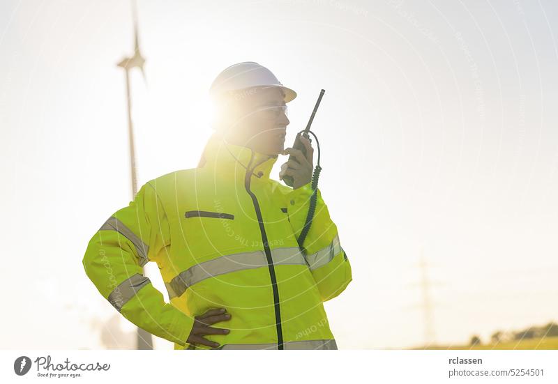 Ingenieurin mit Sicherheitsweste, die ein Walkie-Talkie benutzt, um eine Windkraftanlage in einem neuen Energiepark zu überprüfen Maschinenbau Feld Elektrizität