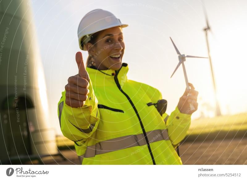 Ingenieurin hält Windturbinenmodell und Daumen hoch in einem Windpark. Neue Energie Konzept Bild Sicherheitsweste Schutzhelm Frau Bauernhof Turbine Techniker