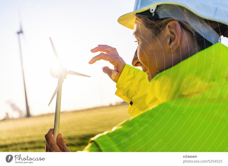 Ingenieurin hält Windturbinenmodell gegen die Sonne. Neue Energie Konzept Bild Sonnenuntergang Sicherheitsweste Schutzhelm Frau Bauernhof Turbine Techniker