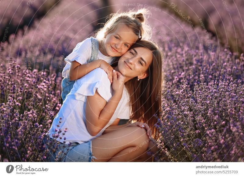 Glückliche Familie in lila Lavendelfeld. junge schöne Mutter und Kind Mädchen genießen zu Fuß blühende Wiese am Sommertag. Mama hat Spaß mit hübschen Tochter in der Natur auf Sonnenuntergang.