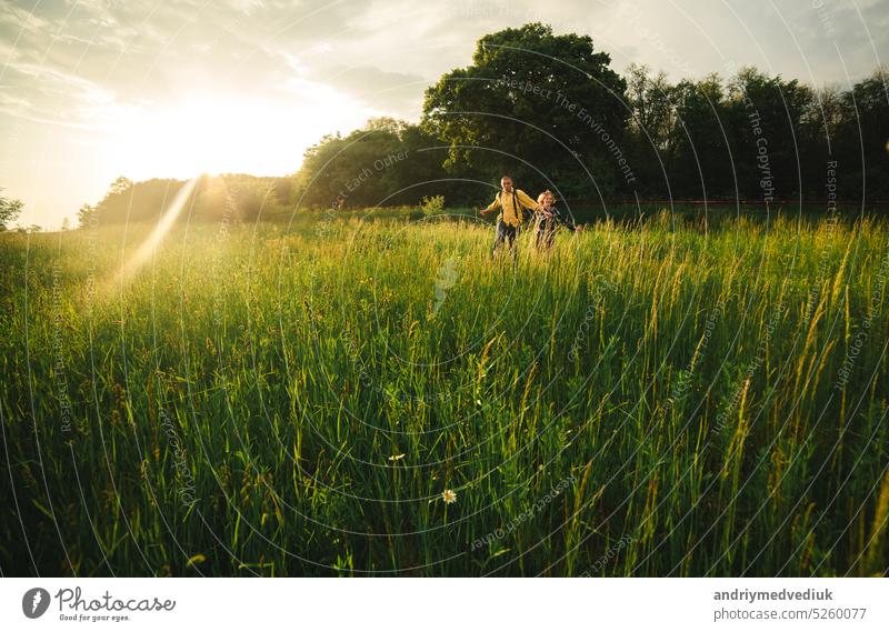 Verliebtes Hipster-Paar, das im Feld spazieren geht, sich küsst und die Hände hält, sich umarmt, im Sommer bei Sonnenuntergang im Gras liegt. valentines day