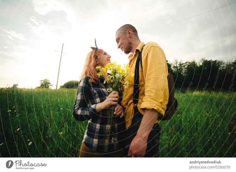 Blumenstrauß aus Wildblumen in der Hand der Frau. Loving Hipster Paar zu Fuß im Feld, küssen und halten die Hände, umarmen, liegen im Gras im Sommer bei Sonnenuntergang. valentines day