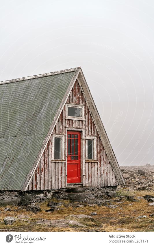 Altes dreieckiges Holzhaus an einem bewölkten Tag Gebäude Haus Außenseite Fassade schäbig hölzern Gelände trist Dreieck Konstruktion Cottage felsig Tür alt