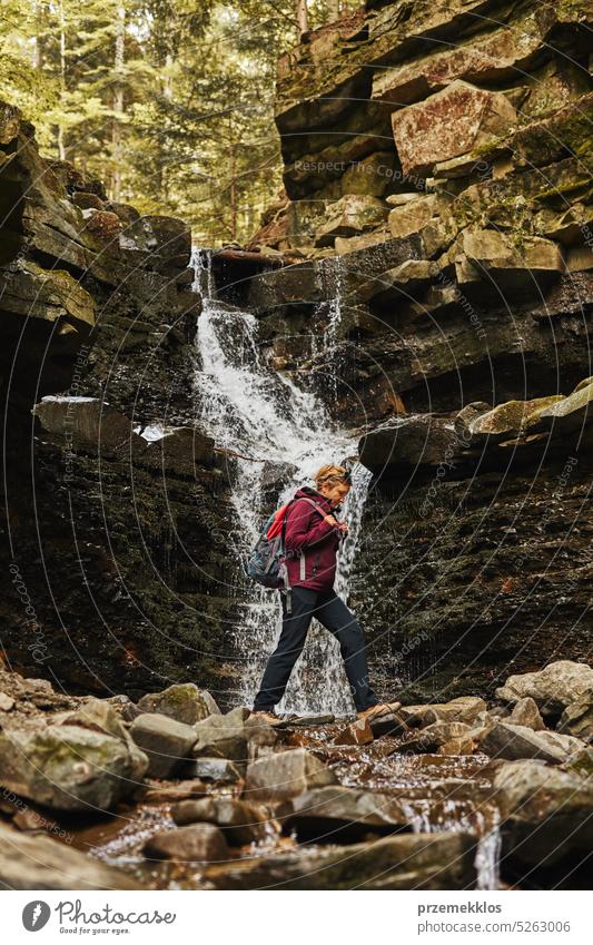 Wandern in den Bergen. Frau genießt Wanderung am sonnigen Urlaubstag. Frau mit Rucksack zu Fuß in der Nähe von Wasserfall. Verbringen Sommerurlaub in der Nähe der Natur