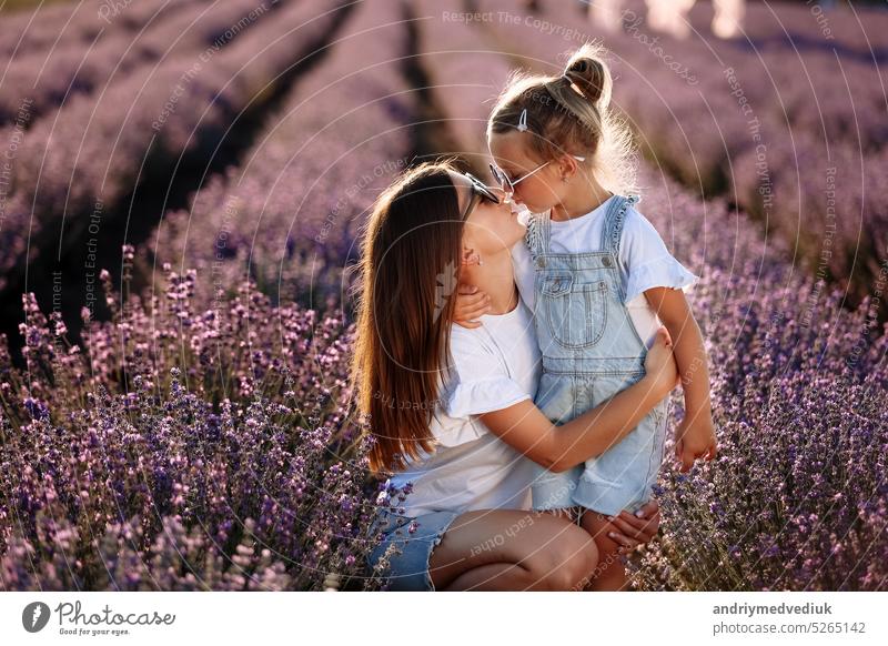 Glückliche Familie in lila Lavendelfeld. junge schöne Mutter und Kind Mädchen genießen zu Fuß blühende Wiese am Sommertag. Mama hat Spaß mit hübschen Tochter in der Natur auf Sonnenuntergang.