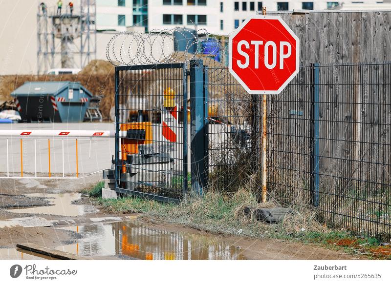 Rotes Stoppschild vor einer Schranke, Zaun und Stacheldraht, Hausfassaden rot leuchtend Baustelle Platz Pfütze Fassaaden Stadt Befehl anhalten Sperre Zugang