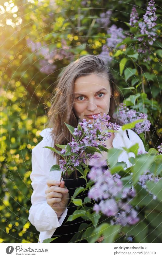 unwirklich schöne junge Frau zu Fuß in einem grünen blühte im Frühjahr in einem Lavendelgarten mit einem Blumenstrauß von Flieder in den Händen. Closeup Mode romantisches Porträt. riechen die Blumen