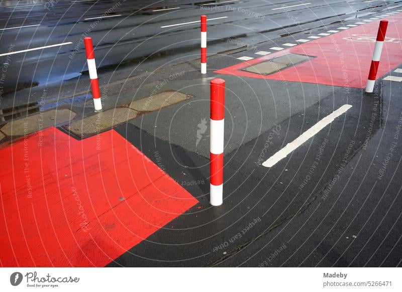 Fahrbahnmarkierung in rot und weiß auf grauem Asphalt für den Radweg mit Poller nach Regen im Sonnenschein auf der Hanauer Landstraße im Ostend von Frankfurt am Main in Hessen