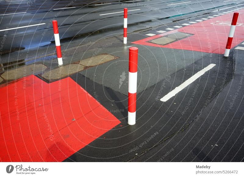 Fahrbahnmarkierung in rot und weiß auf grauem Asphalt für den Radweg mit Poller nach Regen im Sonnenschein auf der Hanauer Landstraße im Ostend von Frankfurt am Main in Hessen