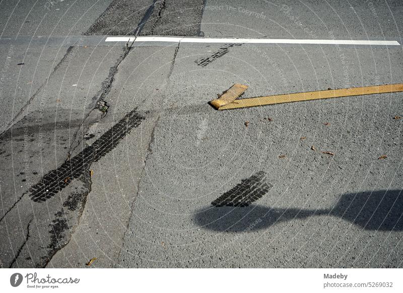 Abgelöste gelbe Fahrbahnmarkierungsfolie auf grauem Asphalt bei Sonnenschein auf einer Baustelle in der Innenstadt von Wuppertal im Bergischen Land Straße Folie