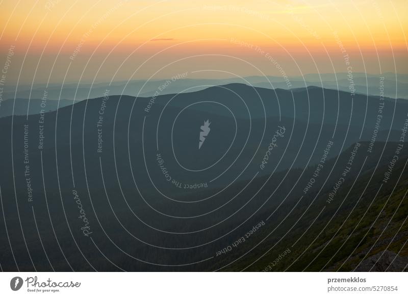 Sonnenaufgang in den Bergen. Natürliche Berglandschaft mit beleuchteten nebligen Gipfeln, nebligen Hängen und Tälern, blauer Himmel mit orange-gelbem Sonnenlicht