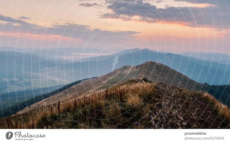 Sonnenuntergang in den Bergen. Natürliche Berglandschaft mit beleuchteten nebligen Gipfeln, nebligen Hängen und Tälern, blauer Himmel mit orange-gelbem Sonnenlicht