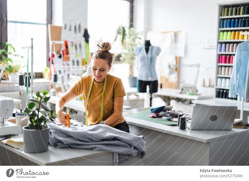 Junge Modedesignerin bei der Arbeit an ihrem Arbeitsplatz Handwerk Schneidern Herstellung handgefertigt Näherin Kleinunternehmen Nähmaschine Werkstatt Gewebe