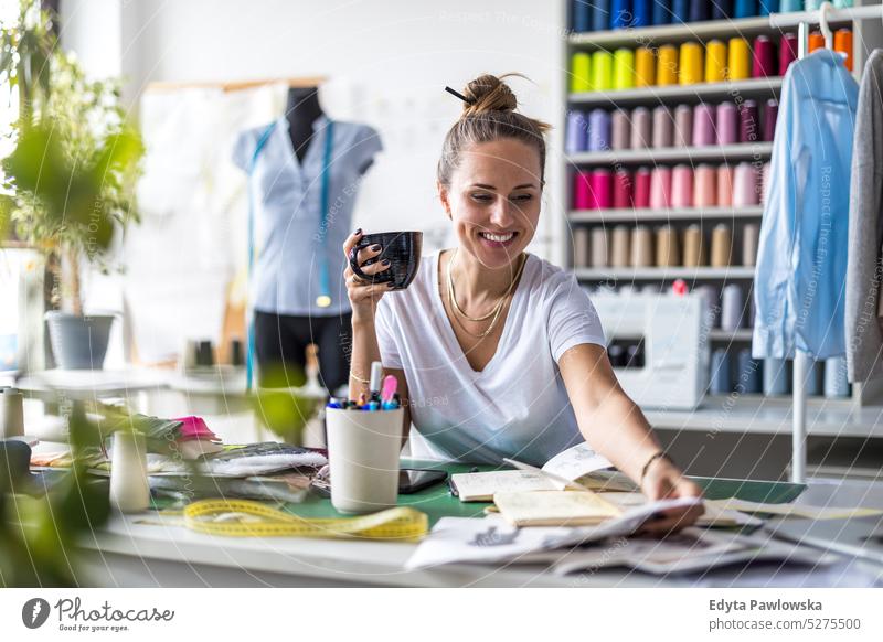 Junge Modedesignerin bei der Arbeit an ihrem Arbeitsplatz Handwerk Schneidern Herstellung handgefertigt Näherin Kleinunternehmen Nähmaschine Werkstatt Gewebe