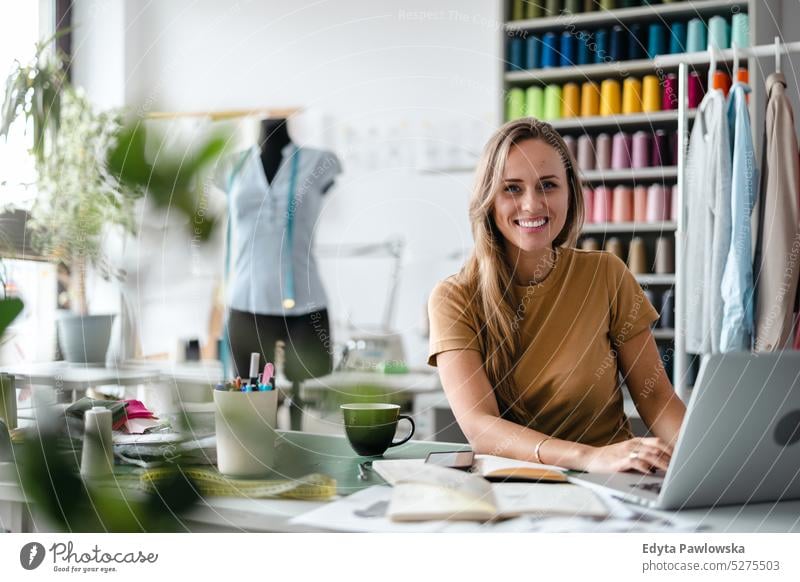 Junge Modedesignerin bei der Arbeit an ihrem Arbeitsplatz Handwerk Schneidern Herstellung handgefertigt Näherin Kleinunternehmen Nähmaschine Werkstatt Gewebe