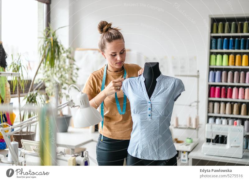 Junge Modedesignerin bei der Arbeit an ihrem Arbeitsplatz Handwerk Schneidern Herstellung handgefertigt Näherin Kleinunternehmen Nähmaschine Werkstatt Gewebe