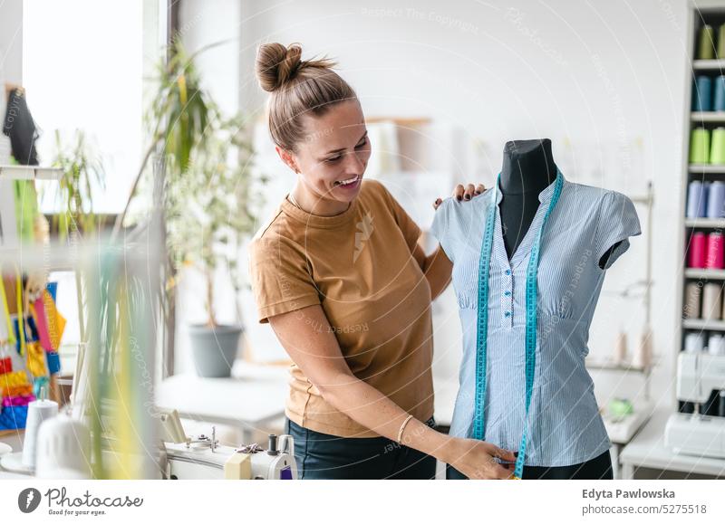 Junge Modedesignerin bei der Arbeit an ihrem Arbeitsplatz Handwerk Schneidern Herstellung handgefertigt Näherin Kleinunternehmen Nähmaschine Werkstatt Gewebe