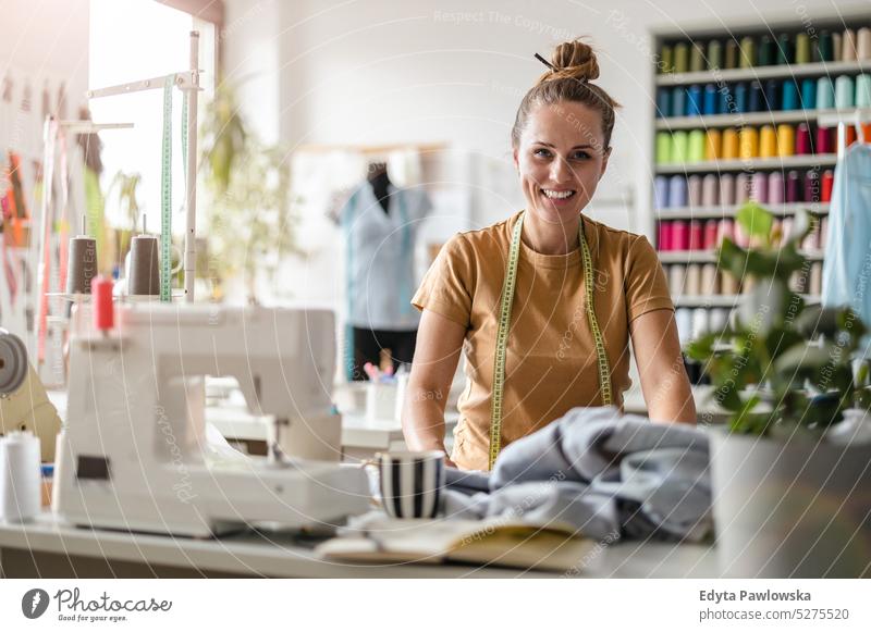 Junge Modedesignerin bei der Arbeit an ihrem Arbeitsplatz Handwerk Schneidern Herstellung handgefertigt Näherin Kleinunternehmen Nähmaschine Werkstatt Gewebe