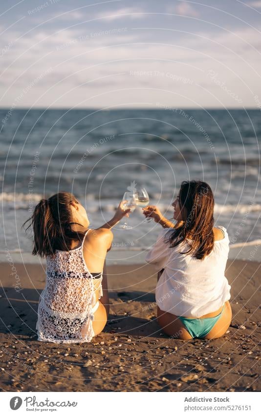 Freundinnen stoßen mit Gläsern am Meer an Frauen Paar Strand Wein Klirren Zuprosten romantisch Abend MEER lesbisch jung Weinglas Zusammensein Liebe lgbt Resort