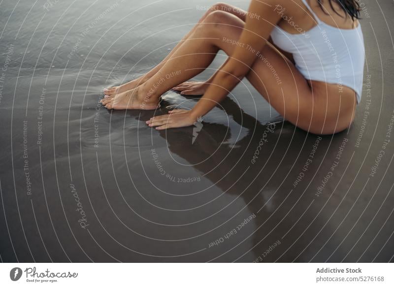 Crop Frau sitzt auf nassem Sand Strand MEER Sommer Wochenende Wasser Urlaub Resort Badebekleidung sitzen Meer Ufer Badeanzug Küste marin Tourismus allein Barfuß