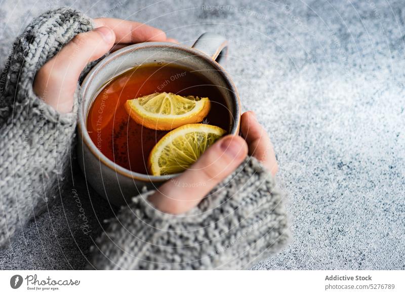 Kinderhände halten eine Tasse Tee Hintergrund Getränk schwarz Zitrusfrüchte Nelken kalte Jahreszeit Beton lecker trinken grau Hand Gesundheit Halt heiß stricken