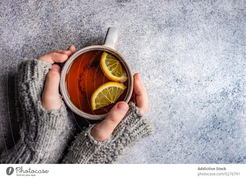 Kinderhände halten eine Tasse Tee Hintergrund Getränk schwarz Zitrusfrüchte Nelken kalte Jahreszeit Beton lecker trinken grau Hand Gesundheit Halt heiß stricken