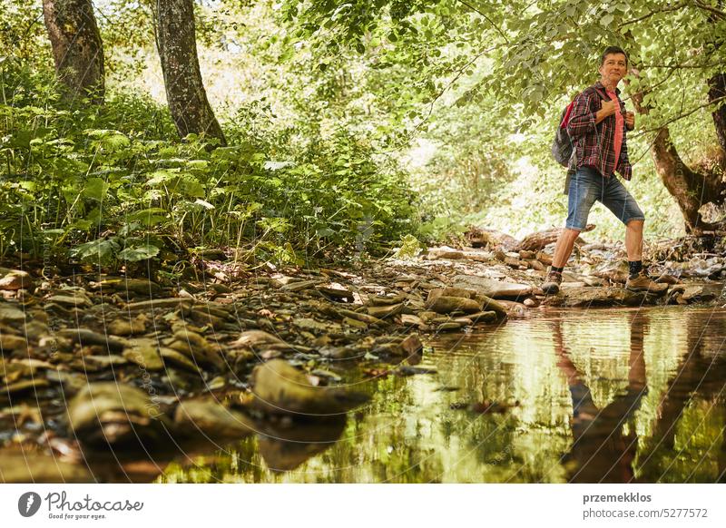 Trekking mit Rucksack Konzeptbild. Backpacker in Trekking-Stiefel überqueren Berg Fluss. Mann Wandern in den Bergen während der Sommerreise Abenteuer reisen