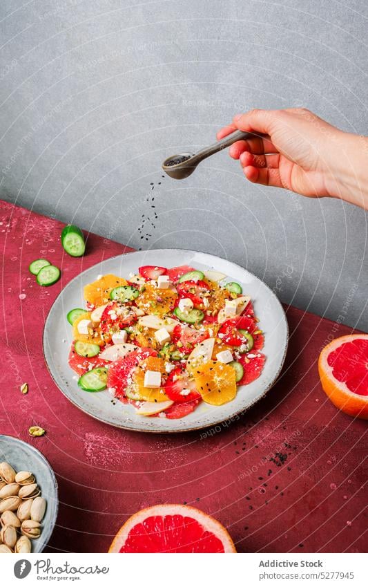 Erntearbeiter, der dem Salat Samen hinzufügt Person hinzufügen Chia Salatbeilage Löffel Käse orange Erdbeeren Salatgurke Teller Gesundheit Frucht