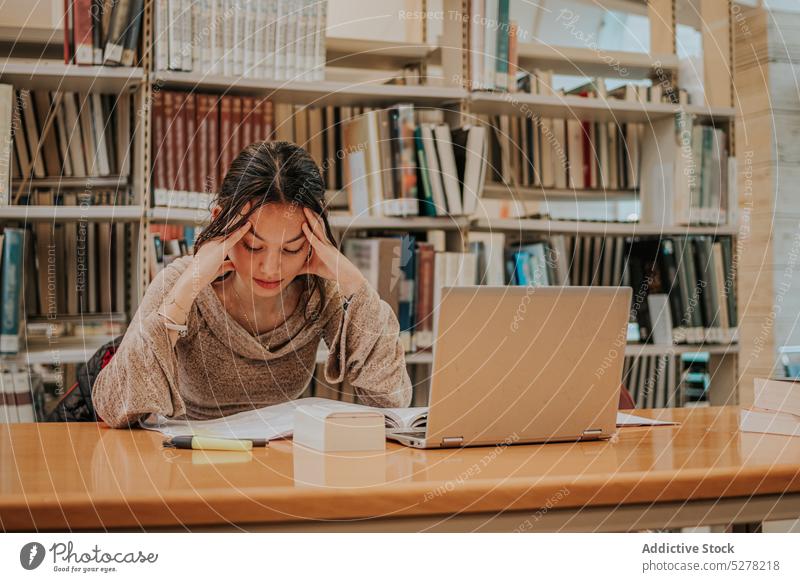 Nachdenkliche Studentin liest ein Buch in der Bibliothek Frau lesen Schüler lernen Laptop Bildung Hausaufgabe Prüfungsvorbereitung Wissen forschen nachdenklich