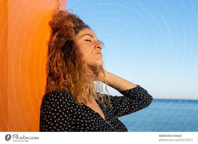 Nachdenkliche Frau, die ihr lockiges Haar am Meer berührt Haare berühren krause Haare Freiheit MEER Wind Straße Sommer Sonnenlicht Freizeit Individualität